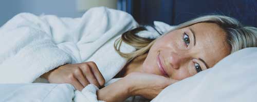 How to sleep better as a light sleeper. Woman who is a light sleeper lies awake.