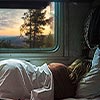 woman laying on her side in an rv with a sheet over top of her and head on pillow