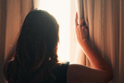 woman at RV window opening blackout curtains and sunlight coming in