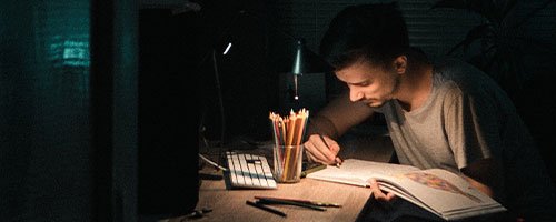 man working at desk in a dark room with work light