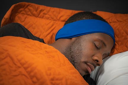 man sleeping with blue SleepPhones Wireless headphones on and orange comforter and pillow