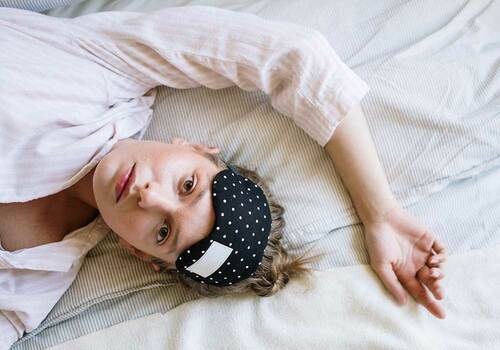 woman in bed in pajamas and black and white polka dot sleep mask