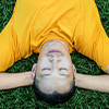 man laying in grass field with eyes shut and head on arms to relax