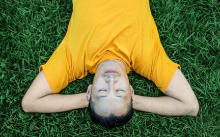 man relaxing in grass field with eyes shut and head on arms