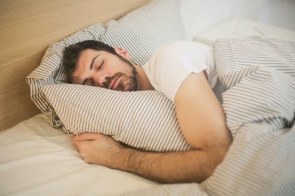 relaxed man sleeping in bed with striped covers