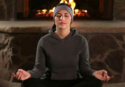 woman sitting in front of fire place cross legged yoga position, eyes closed with SleepPhones headband headphones on practicing quantum healing with self hypnosis