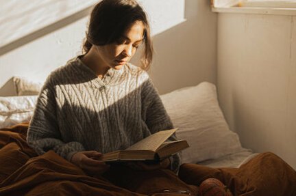 Tired woman with ptsd can't sleep sitting up in bed reading book
