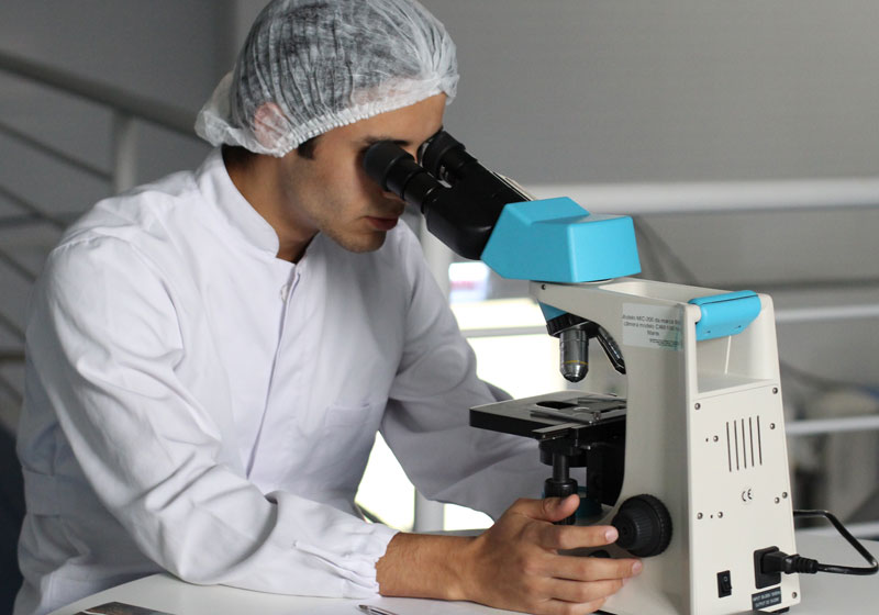 Lab researcher looking through microscope at coronavirus