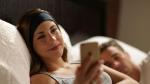 woman smiling in bed while using smart device coupled with sleepphones headphones