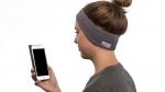 woman holding smartphone while wearing sleepphones in soft gray fleece